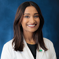 Woman with shoulder length dark hair wearing a black shirt and white coat with UT Southwestern logo